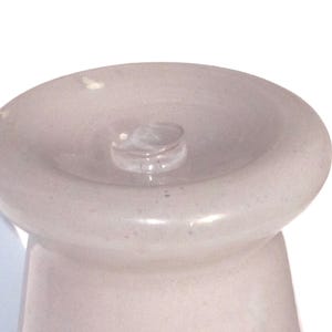 May include: A light pink bottle stopper with a rounded top and a small, clear glass stopper in the center. The stopper has a smooth, glossy finish and a slightly textured appearance. The design is simple and elegant.