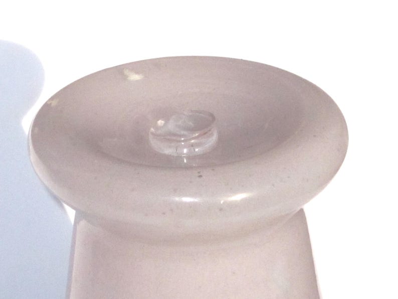May include: A light pink bottle stopper with a rounded top and a small, clear glass stopper in the center. The stopper has a smooth, glossy finish and a slightly textured appearance. The design is simple and elegant.