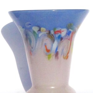 May include: A decorative glass vase with a flared top and a rounded base. The top is a light blue, transitioning to a pale pink body. The vase features colorful, abstract swirls of red, green, and blue near the top.