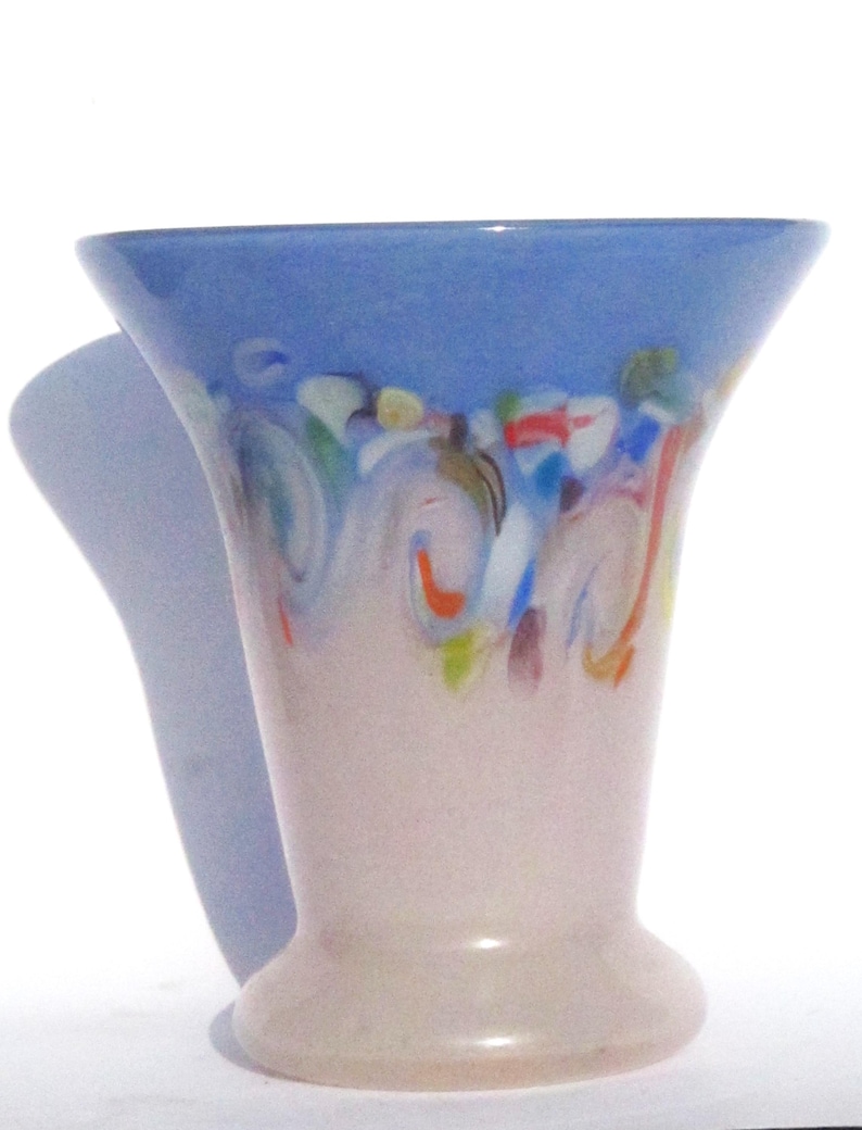 May include: A decorative glass vase with a flared top and a rounded base. The top is a light blue, transitioning to a pale pink body. The vase features colorful, abstract swirls of red, green, and blue near the top.