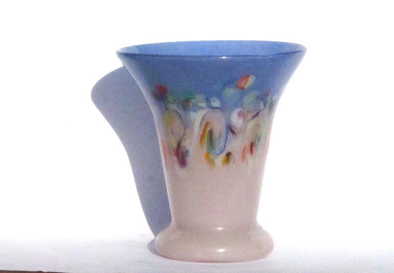 May include: A decorative vase with a flared top and a rounded base. The top is a light blue, transitioning to a pale pink base. Colorful abstract paint strokes adorn the upper portion of the vase.