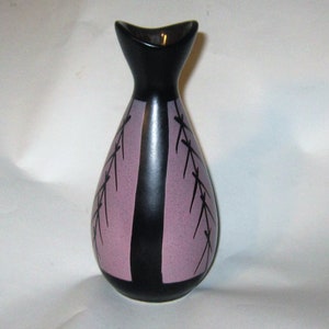 Peut inclure: Un vase en céramique noire avec un motif géométrique rose et noir. Le vase a une large ouverture et une base étroite.