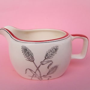 May include: A white ceramic creamer with a red rim and a black and white wheat design.