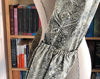 May include: A gray and white paisley patterned yoga mat carrier with a drawstring closure. The carrier is made of fabric and has a gathered bottom.