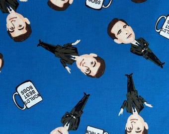May include: A blue fabric featuring a repeating pattern of a cartoon man in a black suit and white shirt, interspersed with white coffee mugs that have the text "WORLD'S BEST BOSS" printed in black on the side of each mug.