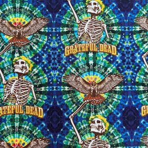 May include: A fabric print featuring a repeating pattern of skeletons with raised arms and eagles with spread wings against a blue, green, and yellow tie-dye background. The text Grateful Dead is printed in yellow letters below each skeleton.