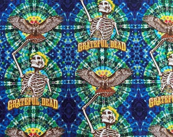 Puede incluir: Un estampado de tela con un patrón repetitivo de esqueletos con los brazos levantados y águilas con las alas extendidas sobre un fondo tie-dye azul, verde y amarillo. El texto Grateful Dead está impreso en letras amarillas bajo cada esqueleto.