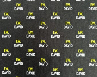 May include: A black fabric featuring a repeating pattern of the text EW, DAVID printed in a yellow and white font. The words are arranged in a grid-like layout across the entire surface of the material, creating a consistent graphic design.