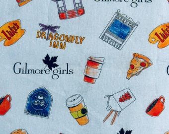 May include: A light blue fabric featuring a repeating pattern of Gilmore Girls themed icons including the text Gilmore Girls, Luke's signs, coffee cups, gazebos, Dragonfly Inn logos, pizza slices, takeout boxes, and burgers in various colors.