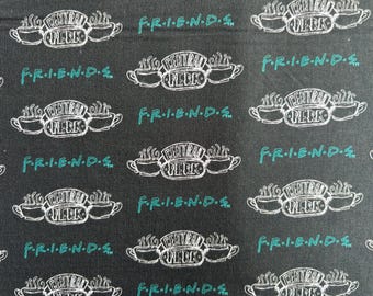 May include: A black fabric featuring a repeating pattern of the white Central Perk logo with two steaming coffee cups and the teal text F.R.I.E.N.D.S. The design is arranged in a grid-like layout across the surface of the textile material.