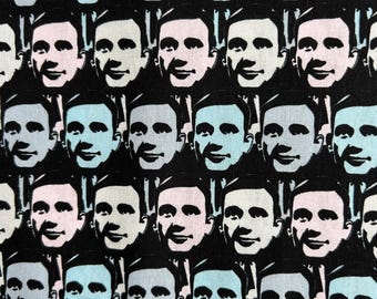 May include: A fabric pattern featuring a repeating grid of stylized male faces in a high-contrast graphic style. The faces alternate between light blue and pale pink tones against a solid black background, creating a uniform and repetitive visual design.