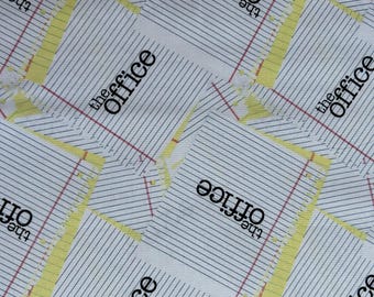 May include: A white fabric featuring a repeating pattern of lined yellow legal notepad paper. Each notepad graphic includes the black text "the office" printed in a bold, sans-serif font, with thin horizontal black lines and a vertical red margin line.