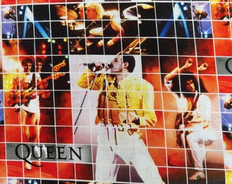 May include: A fabric print featuring a grid overlay of the rock band Queen performing on stage. The design includes multiple concert images of the band members, including a central figure in a yellow jacket, with the word QUEEN printed in black.