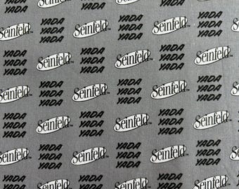 May include: A gray fabric featuring a repeating pattern of the black Seinfeld logo inside an oval shape, interspersed with the word YADA printed in a bold, black, slanted sans-serif font throughout the entire surface of the material.