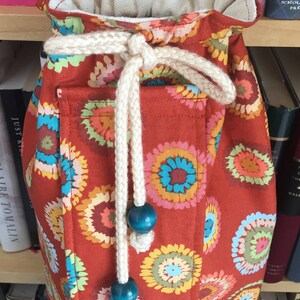 Puede incluir: Una bolsa de cord&oacute;n roja con un cord&oacute;n blanco y cuentas azules. La bolsa tiene un patr&oacute;n floral con c&iacute;rculos coloridos.