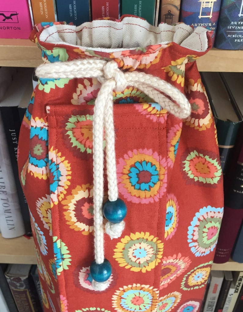 Puede incluir: Una bolsa de cord&oacute;n roja con un cord&oacute;n blanco y cuentas azules. La bolsa tiene un patr&oacute;n floral con c&iacute;rculos coloridos.