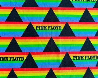 May include: A fabric pattern featuring horizontal rainbow stripes in red, orange, yellow, green, blue, and violet, interspersed with solid black triangles. The text PINK FLOYD is printed in black capital letters across some of the rainbow sections.