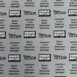 May include: A light gray fabric featuring a repeating pattern of black text and logos. The print includes the Dunder Mifflin Paper Company logo, the text 'the office', and the phrase 'Bears. Beets. Battlestar Galactica. Assistant to the Regional Manager.'