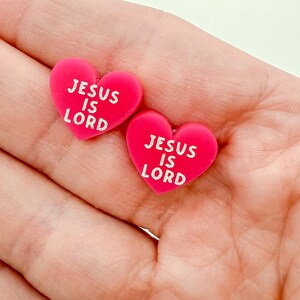 May include: Two bright pink heart-shaped objects with the text "JESUS IS LORD" in white. The hearts are slightly textured and appear to be made of a soft material. The image is a close-up shot.