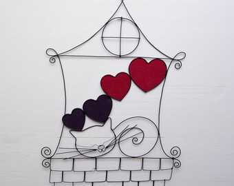 Puede incluir: Escultura de alambre de una casa con un gato en el techo y corazones colgando de la ventana. El gato es blanco y negro y los corazones son rojos y morados.