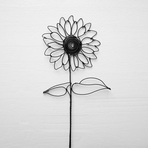 May include: A black wire sunflower sculpture with a single stem and two leaves. The sunflower is made of wire and has a spiral center.