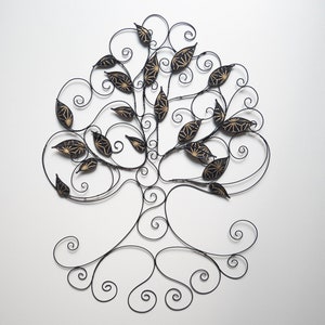 May include: A black metal tree wall decor with gold leaf accents. The tree is made of wire and has a whimsical, organic design.