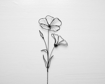 Puede incluir: Una escultura de alambre negro de una flor con dos flores y hojas.