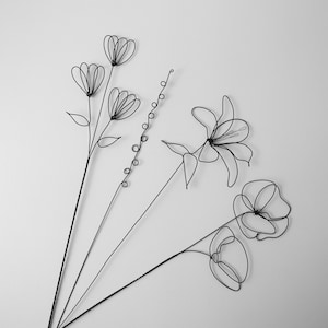 Puede incluir: Un ramo de flores de alambre negro, que incluye un lirio, una amapola y un grupo de flores m&aacute;s peque&ntilde;as. Las flores est&aacute;n dispuestas en un estilo simple y elegante.