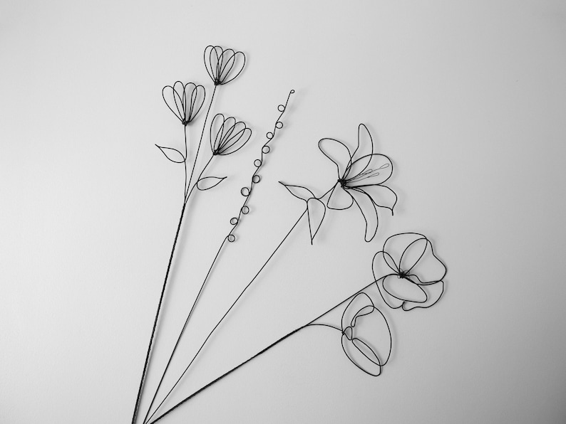 Puede incluir: Un ramo de flores de alambre negro, que incluye un lirio, una amapola y un grupo de flores m&aacute;s peque&ntilde;as. Las flores est&aacute;n dispuestas en un estilo simple y elegante.