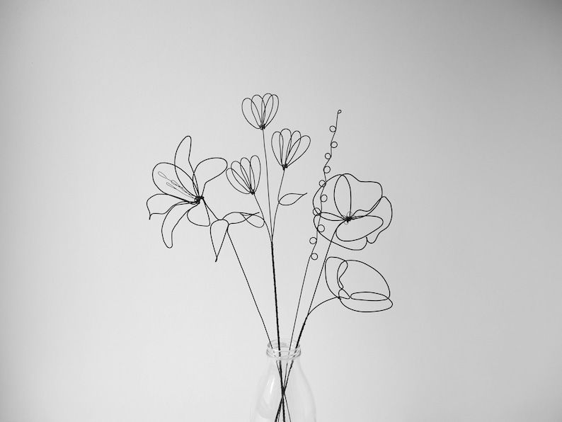 Puede incluir: Un ramo de flores de alambre negro en un jarr&oacute;n de vidrio transparente. Las flores son estilizadas e incluyen un lirio, una amapola y una flor m&aacute;s peque&ntilde;a con forma redondeada.