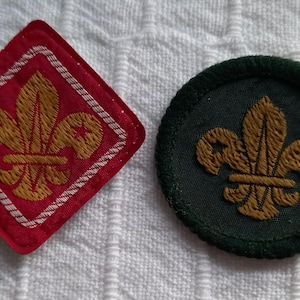 May include: Two embroidered scout badges, one red with white trim and one green. Both badges feature a gold fleur-de-lis.