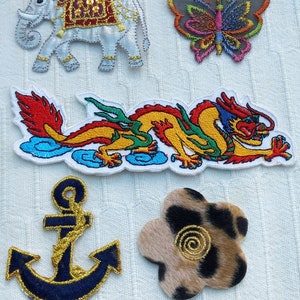 May include: Five embroidered iron-on patches: a white elephant with a red and gold saddle, a multi-coloured butterfly, a yellow and green dragon, a blue anchor with gold trim, and a brown and black flower with a gold swirl.