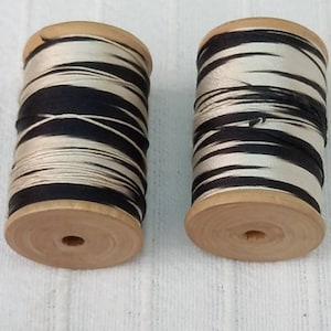 May include: Two spools of black and white striped thread on wooden bobbins.