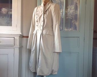 May include: A white, long-sleeved coat with a double-breasted closure and a gathered skirt. The coat is displayed on a white mannequin against a light blue background.