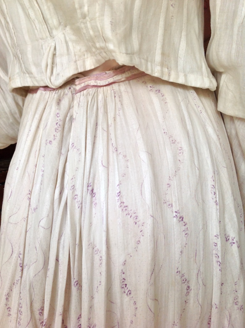 Puede incluir: Un vestido de algod&oacute;n blanco con una cinta de raso rosa y un delicado estampado floral en morado.
