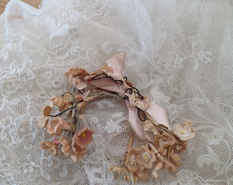 Puede incluir: Una delicada corona de flores secas con una cinta rosa, descansando sobre una tela de encaje blanca.