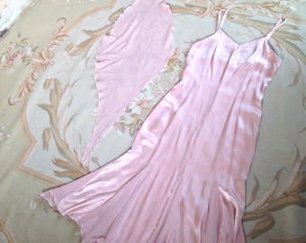 May include: A light pink satin slip dress with spaghetti straps and a flared hem, paired with a matching scarf. The dress and scarf are displayed on a floral patterned rug.