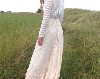 May include: A floor-length dress featuring a white long-sleeved bodice with horizontal sheer stripes and a high neckline. The skirt is a light cream color with a delicate pink floral pattern, finished with tiered ruffled layers at the hemline.