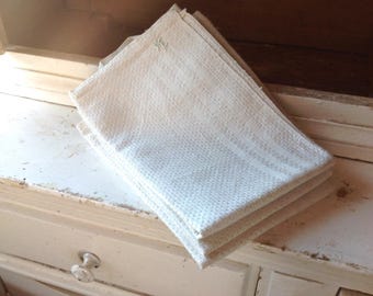 May include: A folded off-white kitchen towel with a textured waffle weave pattern. The fabric features a small, embroidered monogram in the upper corner, consisting of the letters 'F' and 'E' stitched in a light thread against the light background.