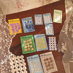 Op de afbeelding: Assortiment van vintage knoopkaarten met verschillende kleuren en patronen. De kaarten bevatten de tekst "Mode Parisienne" en "La Carte" met een blauwe, groene en gele achtergrond. De knoppen zijn gemaakt in Frankrijk.