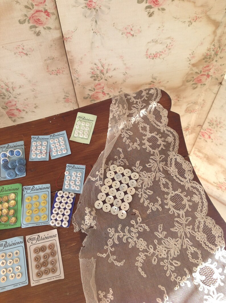 Op de afbeelding: Assortiment van vintage knoopkaarten met verschillende kleuren en patronen. De kaarten bevatten de tekst "Mode Parisienne" en "La Cite" in het Frans. De kaarten worden weergegeven op een houten oppervlak met een kantonderlegger.