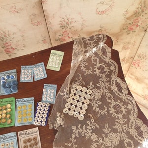 Op de afbeelding: Assortiment van vintage knoopkaarten met verschillende kleuren en patronen. De kaarten dragen de tekst "Mode Parisienne" en worden getoond op een houten oppervlak met een kantdoily.