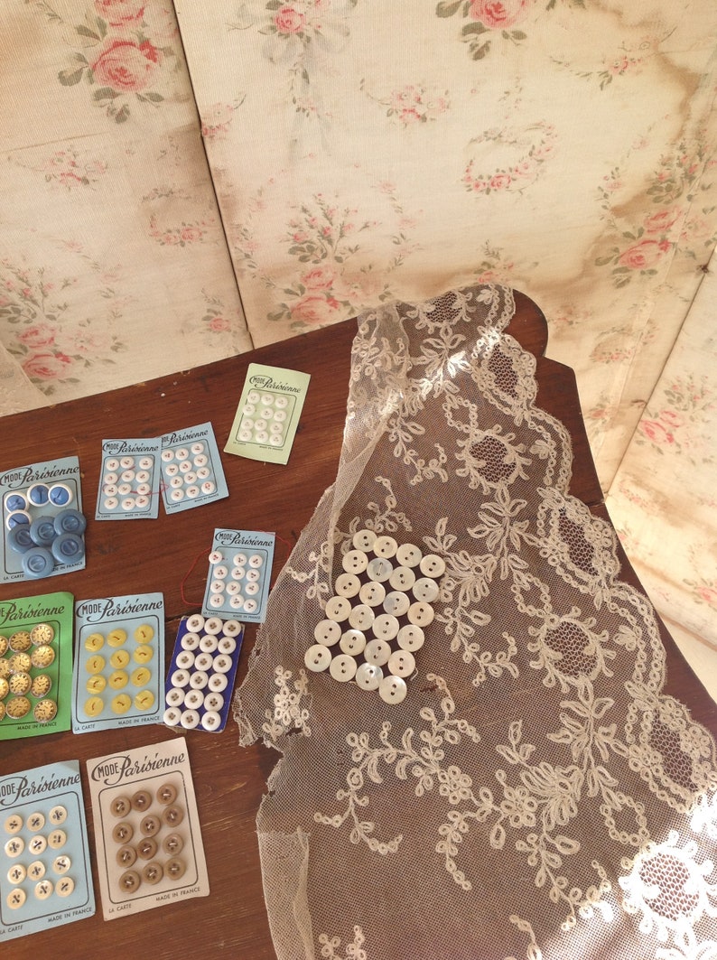 Op de afbeelding: Assortiment van vintage knoopkaarten met verschillende kleuren en patronen. De kaarten dragen de tekst "Mode Parisienne" en worden getoond op een houten oppervlak met een kantdoily.