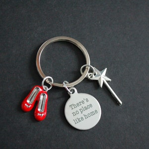 May include: A silver keyring with a round charm that says "There's no place like home". The keyring also has a pair of red ruby slippers and a silver wand with a star on top.