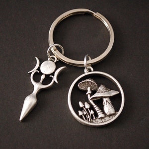 May include: Silver key chain with two charms. One charm is a triple moon goddess with a circle in the centre. The other charm is a circle with a mushroom design.