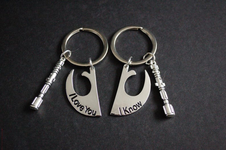 May include: Two silver keyrings with matching pendants. Each pendant is a crescent shape with the phrases "I Love You" and "I Know" engraved. Each keyring also has a small silver lightsaber charm.