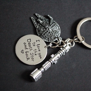 Peut inclure: Porte-clés argenté avec un charme représentant le Faucon Millenium, un charme de sabre laser et un charme rond avec l'inscription "I love you to the Death Star and back". Le porte-clés a un anneau argenté.
