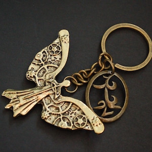May include: A gold-toned metal keychain featuring a detailed angel wing design with a circular charm that says "L2".