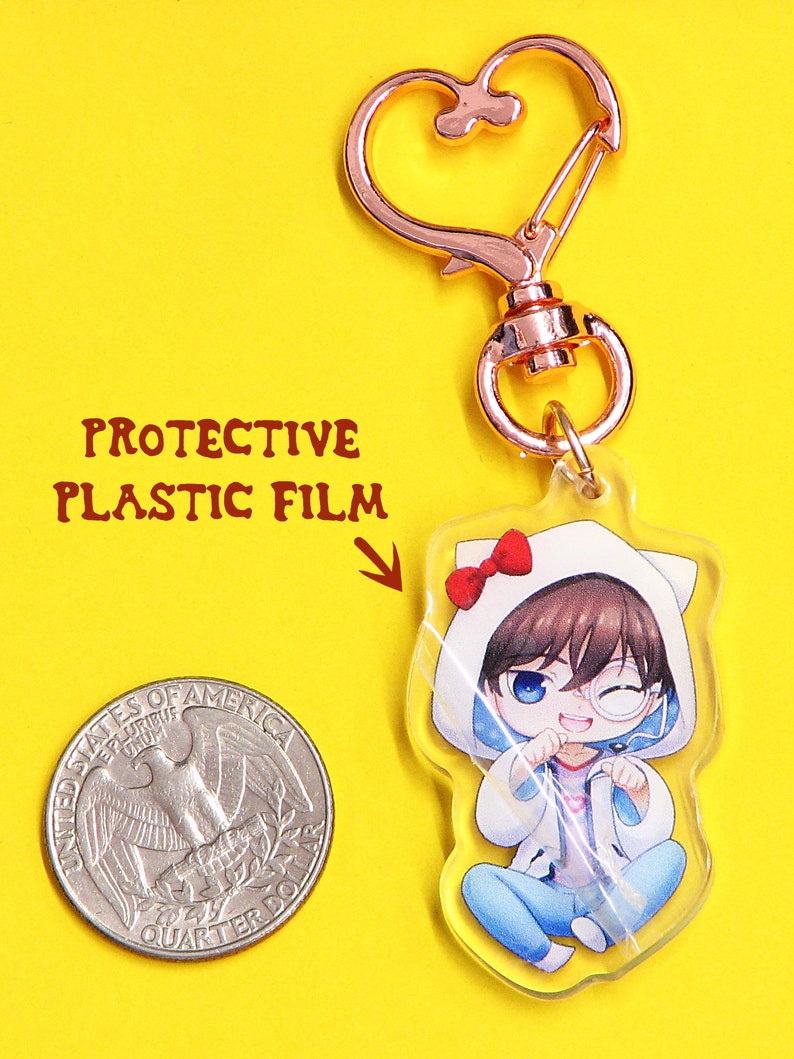 May include: A clear acrylic keychain featuring an anime character with brown hair, wearing a white hooded jacket with a red bow on top, blue jeans, and a white cat ear headband. The keychain has a rose gold metal clasp.