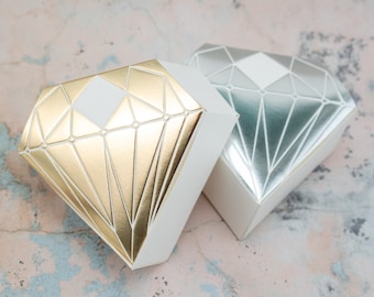 May include: Two diamond-shaped gift boxes, one gold and one silver, with a geometric pattern. The boxes are made of cardboard and have a white interior.